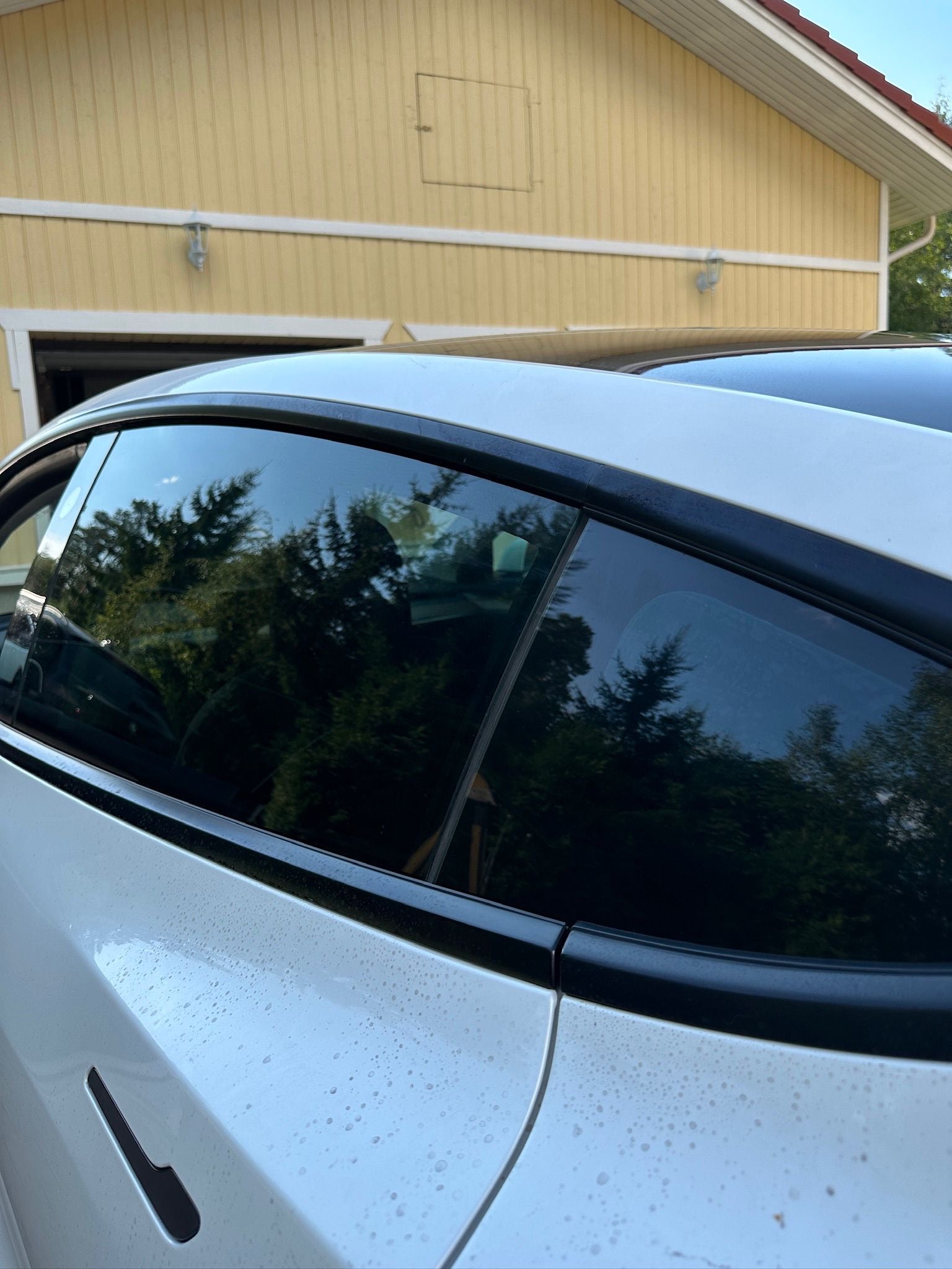 Car parked in front of a yellow building with trees in the reflection.